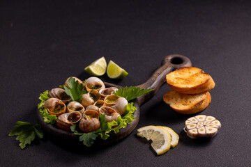 Snails with garlic butter sauce, parsley, and toasted bread on wooden cutting board