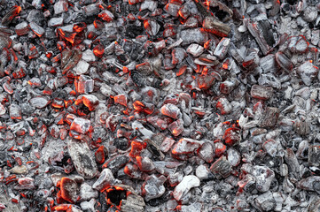 Overhead view of glowing charcoal embers and ash in a barbecue grill. Warm orange coals, textured...