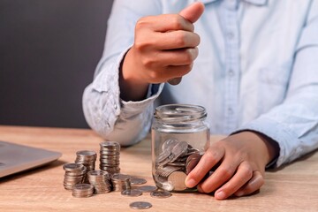 A woman counting and putting coins into a glass jar. Saving money and financial concept.