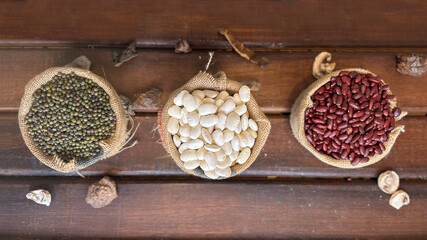 Overhead shot of three small burlap sacks filled with white, red, and pinto beans, placed on a rustic wooden background. Natural, organic food concept 