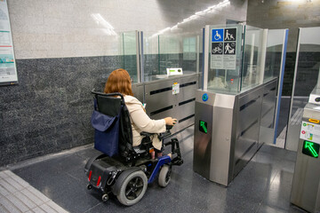 Businesswoman in wheelchair entering subway station through accessible gate. Concept of inclusion
