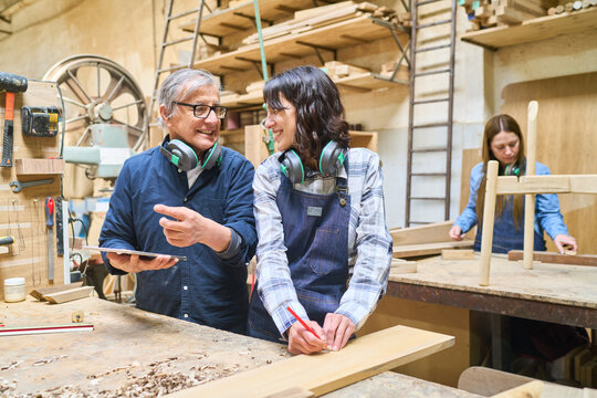 Experienced craftsman teaching young apprentice in a woodworking shop