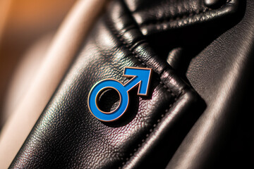 Close-up of blue male gender symbol pin on worn black leather jacket symbolizing masculinity and toxic patriarchy critique