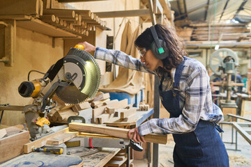 Young woman working with saw in lumberyard workshop