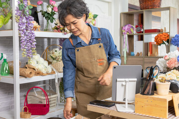 Asian senior woman, florist, small business, owner arranging roses at flower shop table, expressing creativity, passion, cheerful lifestyle, floral service and retirement independence, aging lifestyle