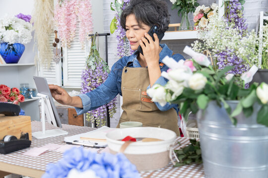 Asian senior woman, florist, small business, owner, entrepreneur manage store accounting with laptop at flower shop, independent lifestyle, creative workspace, passion for business, and modern skills