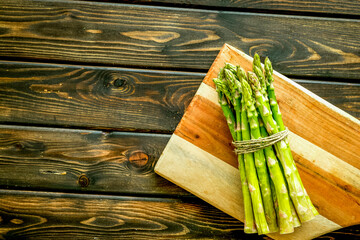 Cooking asparagus. Bunch steams on cutting board on dark wooden background top-down copy space