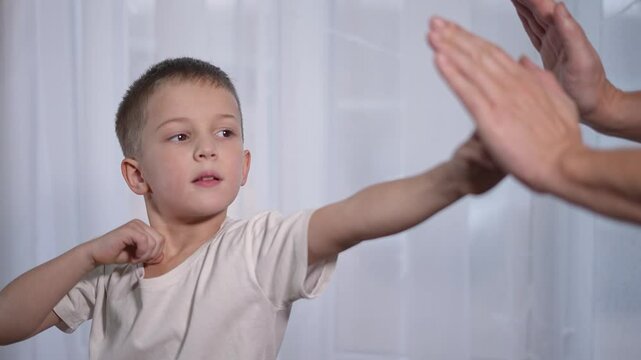 Boy training punching hand with coach. Child learns martial movement. Fitness exercise for child discipline. Punching routine during martial exercise. Learning basic skills with coach guidance