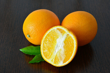 Fresh oranges with a slice on a dark wooden surface close up