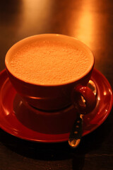 Bubbly hot aroma cappuccino or coffee with whipped milk in the nice red cup taken in warm cafe light 