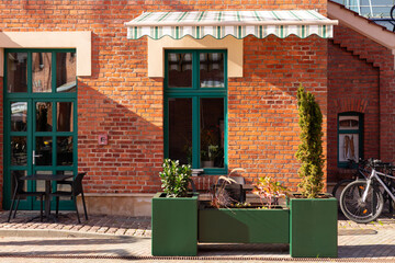 Street cafe with brick walls and canopy exterior design. Front view, sunny day. An outdoor cafe with tables, chairs. Lush green plants growing in pots near house. High quality photo.