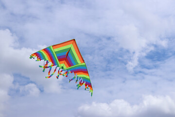Bright kite against the cloudy sky. Toy for children and adults. Outdoor activities. Colorful kite flies in the sky, windy weather. Cloudless mood. Fly. Bright multi-colored kite flies in the air