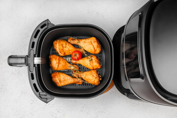 Top view of seasoned chicken drumsticks and a tomato cooking inside a modern black air fryer on a...