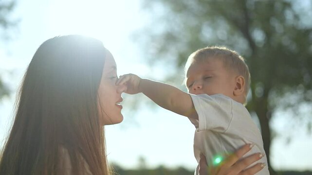 Happy mother holding baby in nature. Mother gently embracing baby outdoors. Joyful bonding moment between mother baby in nature. Emotional connection sunlight. Happy mother enjoying nature with baby.