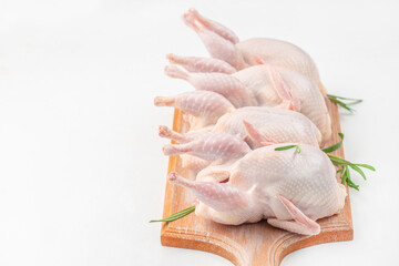 Four raw quails arranged neatly on a wooden cutting board with rosemary sprigs, ready for seasoning...