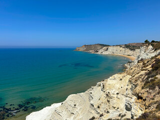 A stunning coastal view with turquoise sea, golden sandy beach, and dramatic white cliffs. The sky is clear and blue, and the coastline curves gracefully, offering a peaceful, picturesque scene.
