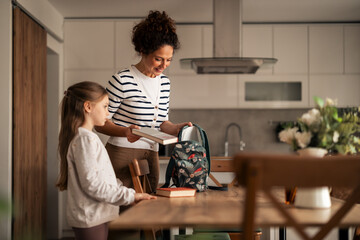 Mother Helping Daughter Pack Books in Backpack for School