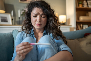 Sad woman holding negative pregnancy test sitting on sofa at home