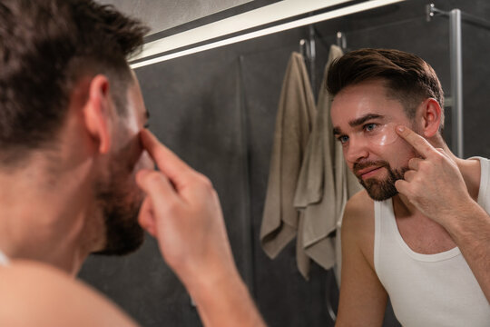 Man applying under eye patches in front of a bathroom mirror - Powered by Adobe