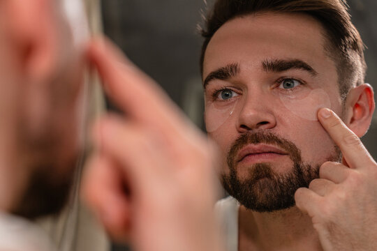 Man applying under eye patches in front of a bathroom mirror