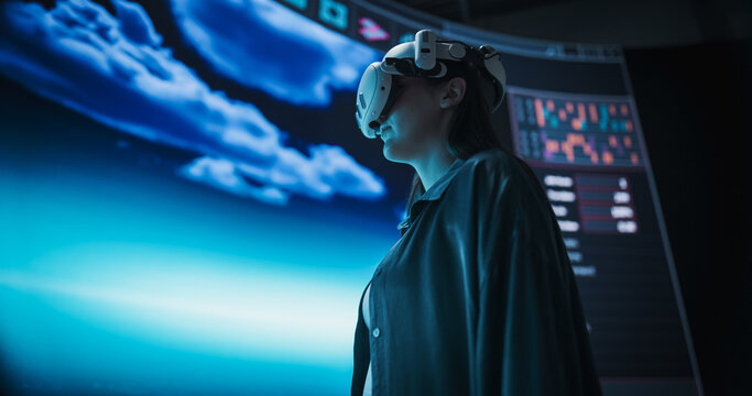Young Woman in VR Headset Crafts Digital Art on a Large Screen, Using Innovative Virtual Reality Design Software and Futuristic Urban Planning. Architecture, Technology and Creativity Concept