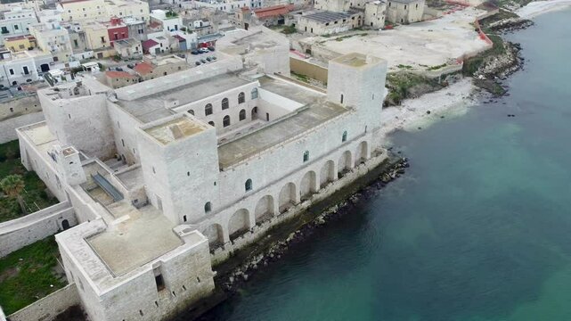 Aerial drone view of Trani, a coastal town in Puglia, Italy, featuring the iconic Trani Cathedral, Castello Svevo, picturesque harbor, and Adriatic Sea shoreline under clear skies.