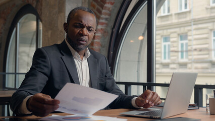 African American entrepreneur typing laptop computer check data in papers dissatisfied problem...
