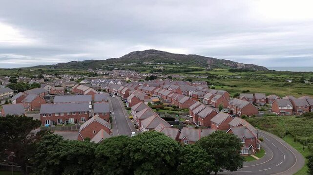 Aerial view orbit across modern red brick housing neighbourhood under Holyhead mountain in Wales
