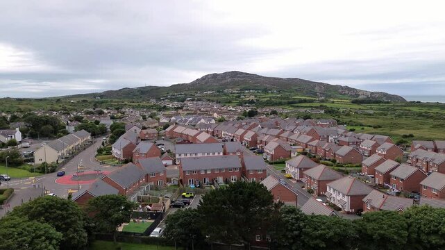Aerial rising view over modern red brick housing neighbourhood under Holyhead mountain in Wales