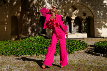 Elegant fashion model in a bold fuchsia feather jacket and jumpsuit with ruffled top and heels...