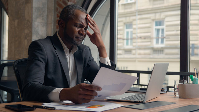 Stressed upset failure paperwork stress problem troubled African American entrepreneur with laptop report check data in papers dissatisfied mistake bad result business man office businessman male guy - Powered by Adobe