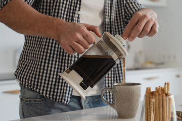 Man  pouring coffee from a French press into a mug in a bright kitchen