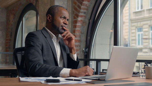 African American ethnic adult employer entrepreneur thinking problem solution hesitate decision ponder think come up with idea man business office businessman male manager guy at table typing laptop - Powered by Adobe