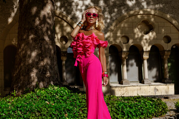Elegant fashion model in a bold fuchsia feather jacket and jumpsuit with ruffled top and heels...