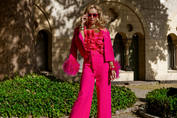Elegant fashion model in a bold fuchsia feather jacket and jumpsuit with ruffled top and heels...