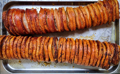 Two long pieces of rolled roasted pork belly, sliced into thick cuts, lie on a metal tray ready for...