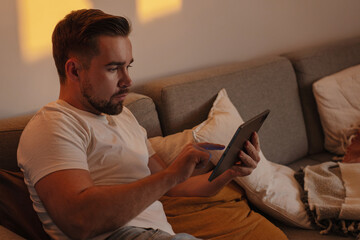 Man Browsing Tablet on Sofa During Cozy Evening at Home