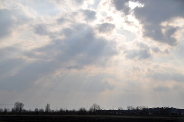 the sun shines through the clouds in single streaks over the field