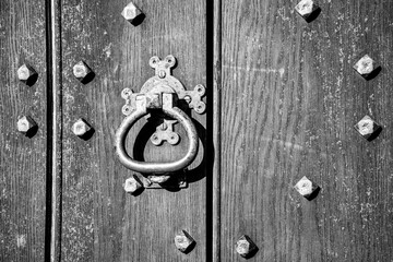 Black and white close-up of an old wooden door with a central, ornate metal door knocker and...