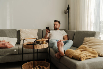 Man Relaxing on Couch at Home with Smartphone and Snacks