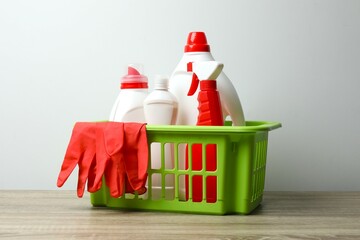Cleaning supplies in green basket on table, with spray, bottles and gloves. Ideal for eco-friendly...