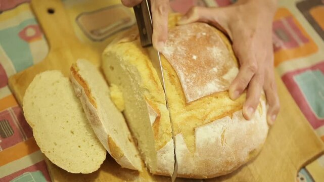 P&atilde;o italiano redondo sendo cortado por m&atilde;os femininas usando uma faca de serra em camera lenta ou slow motion.