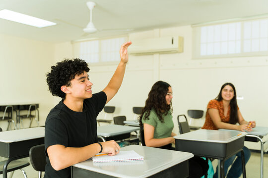 Latin high school student raising hand in classroom to answer question