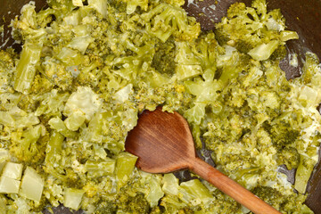 An overhead shot of cooked broccoli florets mixed with a creamy sauce in a dark pan, with a wooden...