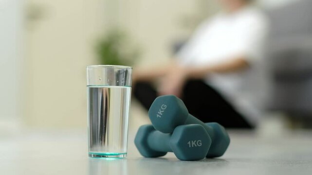 A glass of water sits on a table next to a pair of dumbbells. The dumbbells are labeled 1 kg