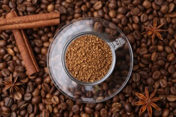 Cup with granulated instant coffee, star anise and cinnamon on beans, top view