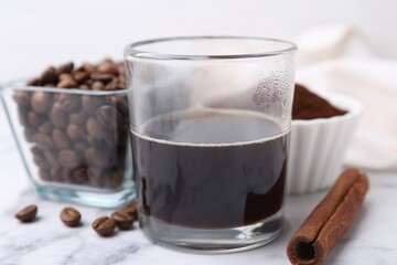 Refreshing coffee in cup, cinnamon stick and beans on white marble table, closeup