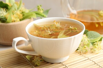Fresh linden tea in cup, teapot and flowers on table, closeup