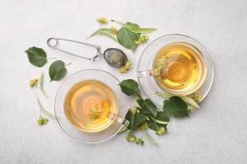 Fresh linden tea in cups and flowers on light grey table, flat lay