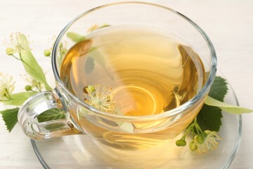 Fresh linden tea in cup and flowers on white wooden table, closeup